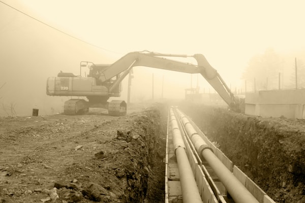 Excavator working alongside large pipes for main line replacement